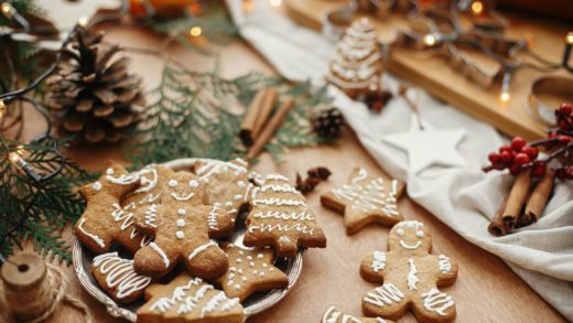 Christmas gingerbread cookies on vintage plate and anise, cinnamon, pine cones, cedar branches with golden lights on rustic table. Baked traditional gingerbread man, tree, star cookies